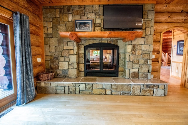 details with wood-type flooring, a stone fireplace, and rustic walls