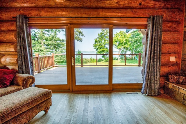 doorway with a healthy amount of sunlight, log walls, and light wood-type flooring