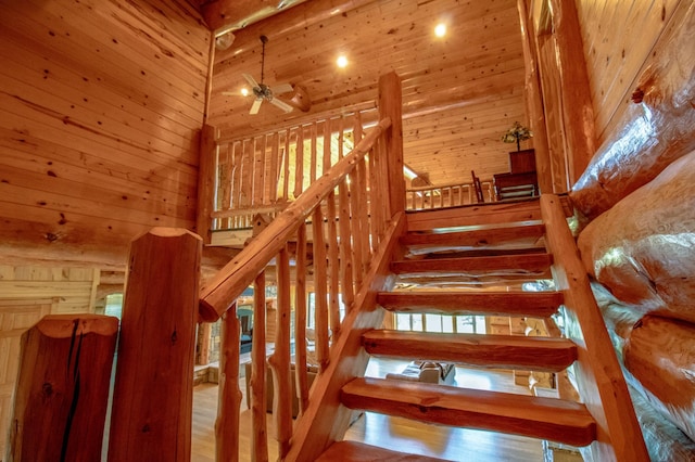 staircase with wood walls, hardwood / wood-style flooring, ceiling fan, wooden ceiling, and a towering ceiling