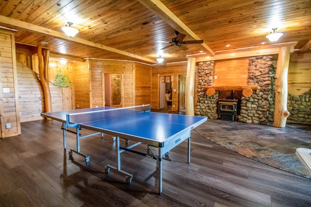 game room featuring ceiling fan, a wood stove, wood walls, and beam ceiling