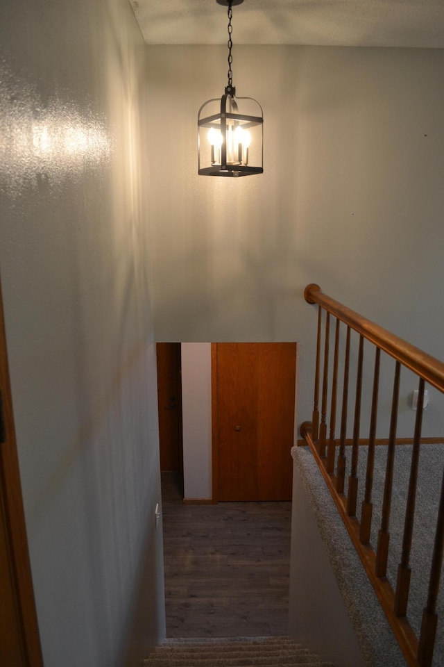 stairway with wood-type flooring and an inviting chandelier