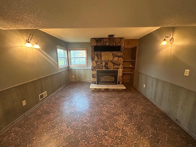 unfurnished living room featuring a textured ceiling, wooden walls, and a fireplace