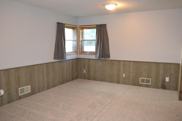 carpeted spare room featuring a textured ceiling and wooden walls