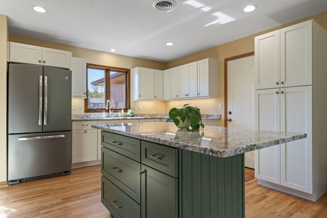 kitchen featuring light stone countertops, a center island, white cabinetry, and stainless steel refrigerator