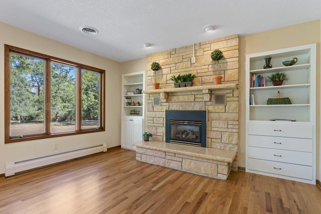 unfurnished living room featuring a fireplace, a baseboard heating unit, a textured ceiling, and light wood-type flooring