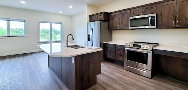 kitchen with sink, light wood-type flooring, stainless steel appliances, dark brown cabinetry, and a center island with sink