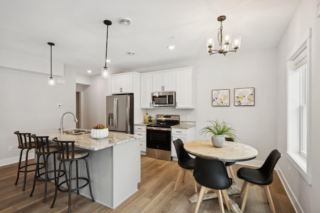 kitchen with appliances with stainless steel finishes, white cabinetry, decorative light fixtures, and a kitchen island with sink