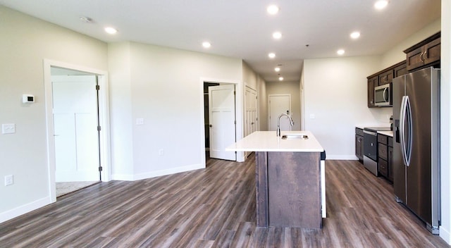 kitchen featuring appliances with stainless steel finishes, a center island with sink, sink, and dark wood-type flooring