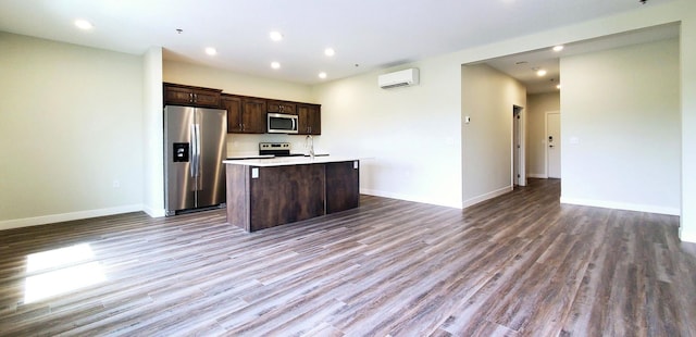 kitchen with an island with sink, a wall mounted AC, hardwood / wood-style flooring, stainless steel appliances, and dark brown cabinets