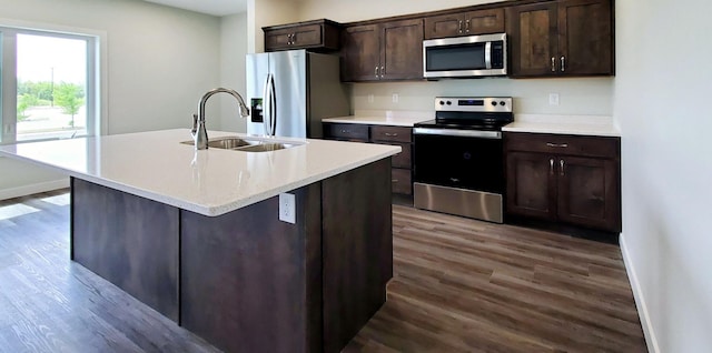 kitchen with sink, appliances with stainless steel finishes, dark brown cabinets, wood-type flooring, and a center island with sink