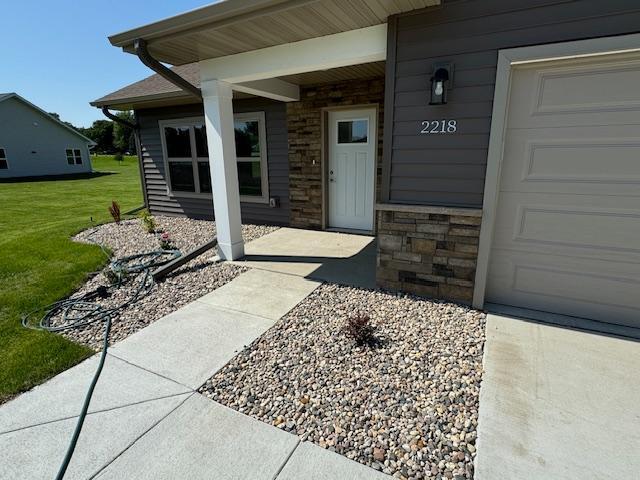 2218 Red Bird Ln, Fairmont, MN 56031 - view of exterior entry featuring stone siding, an attached garage, and a lawn