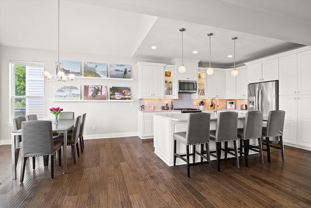 kitchen with appliances with stainless steel finishes, an island with sink, white cabinetry, decorative light fixtures, and dark wood-type flooring