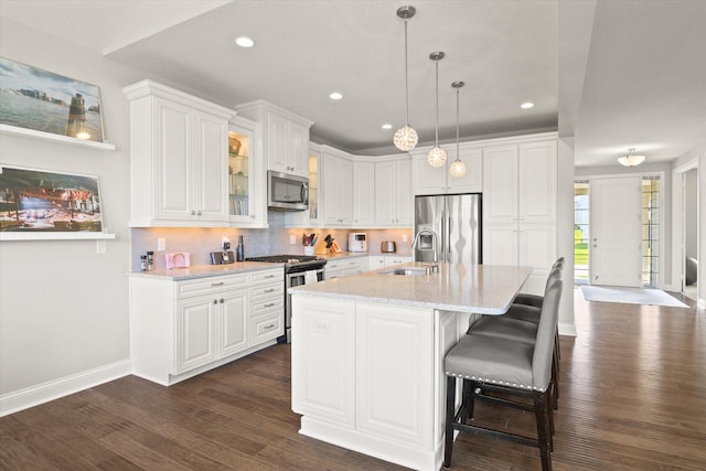 kitchen with light stone countertops, sink, white cabinetry, stainless steel appliances, and decorative light fixtures