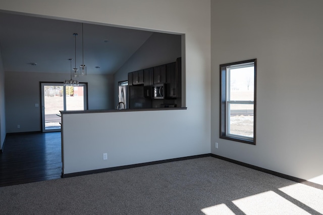 interior space with dark colored carpet, lofted ceiling, a healthy amount of sunlight, and a notable chandelier