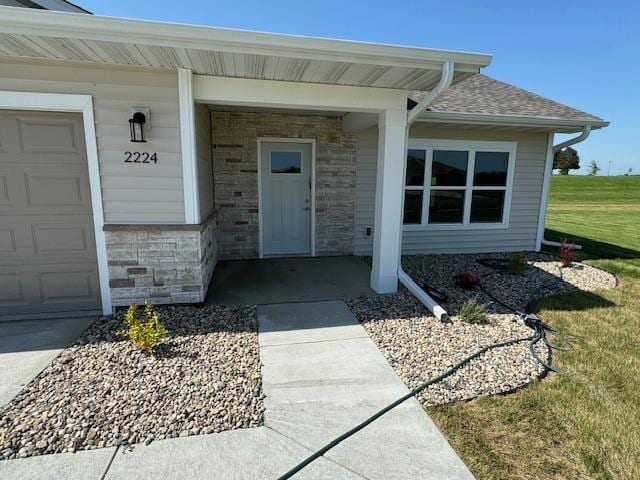 2224 Red Bird Ln, Fairmont, MN 56031 - view of exterior entry featuring stone siding, an attached garage, a lawn, and covered porch
