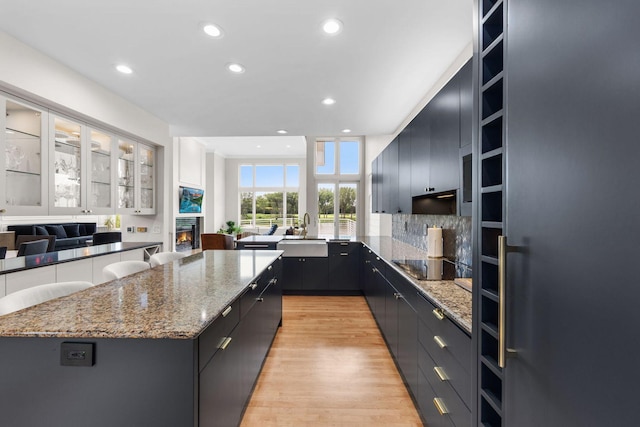 17680 Bearpath Trl, Eden Prairie, MN 55347 - kitchen featuring black electric stovetop, a glass covered fireplace, modern cabinets, light wood-style floors, and recessed lighting
