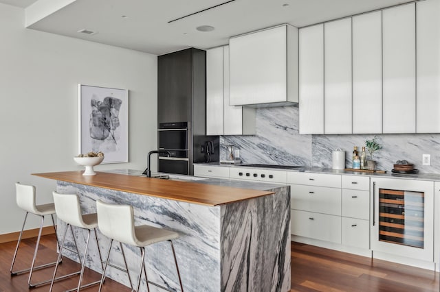 kitchen with an island with sink, beverage cooler, white cabinetry, and sink