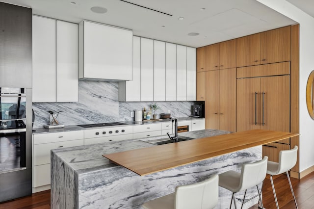 kitchen with stovetop, white cabinetry, dark hardwood / wood-style floors, and a kitchen island with sink