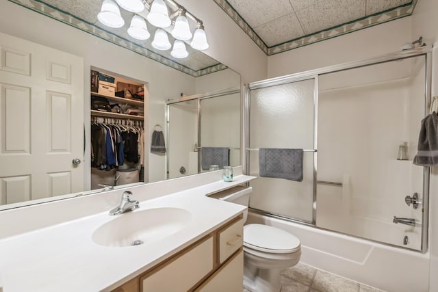 full bathroom featuring tile patterned flooring, a drop ceiling, shower / bath combination with glass door, vanity, and toilet