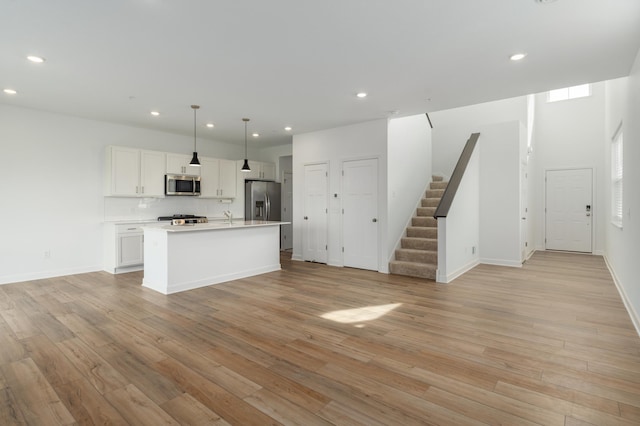 kitchen with appliances with stainless steel finishes, an island with sink, light hardwood / wood-style floors, decorative light fixtures, and white cabinets