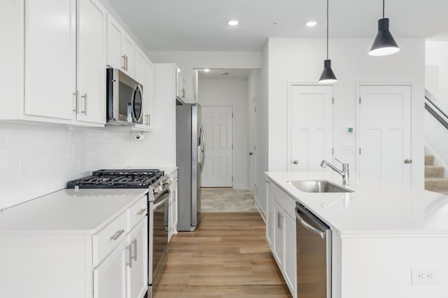 kitchen with light hardwood / wood-style flooring, stainless steel appliances, sink, pendant lighting, and white cabinetry