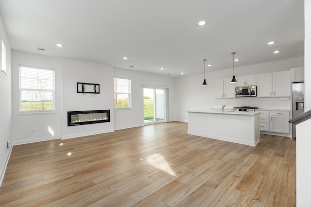 kitchen with appliances with stainless steel finishes, white cabinetry, light hardwood / wood-style floors, pendant lighting, and a center island with sink