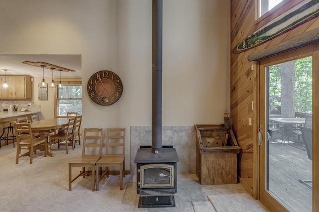 interior space with light carpet, wood walls, a wood stove, and a healthy amount of sunlight