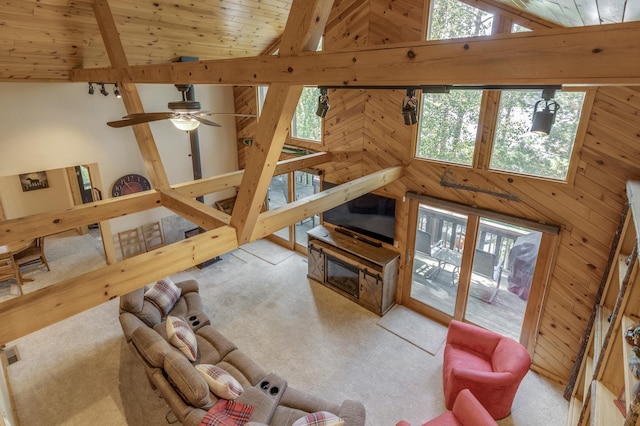 carpeted living room with a healthy amount of sunlight, wood walls, ceiling fan, and high vaulted ceiling