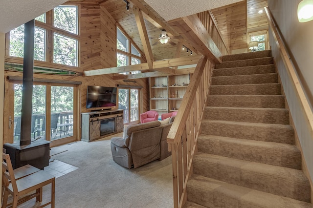 carpeted living room with wood ceiling, high vaulted ceiling, a wood stove, track lighting, and wooden walls