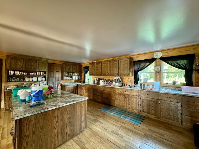 kitchen featuring light wood-type flooring, light stone countertops, a center island, and sink