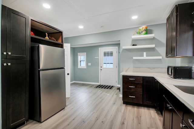 kitchen with light wood-style floors, freestanding refrigerator, open shelves, light stone counters, and baseboards