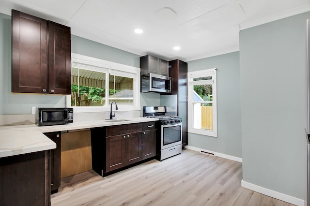kitchen featuring dark brown cabinetry, a sink, stainless steel appliances, light wood finished floors, and baseboards