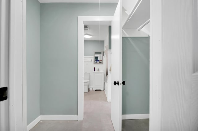 hall featuring attic access, baseboards, and concrete flooring