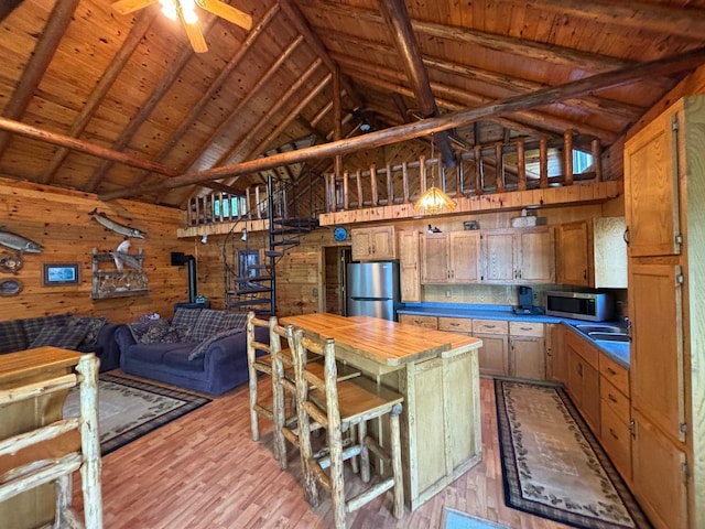 kitchen featuring wooden walls, light wood-type flooring, stainless steel appliances, ceiling fan, and a breakfast bar