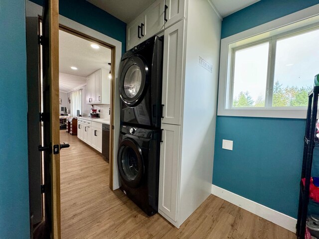 laundry area featuring stacked washing maching and dryer, light hardwood / wood-style flooring, and cabinets