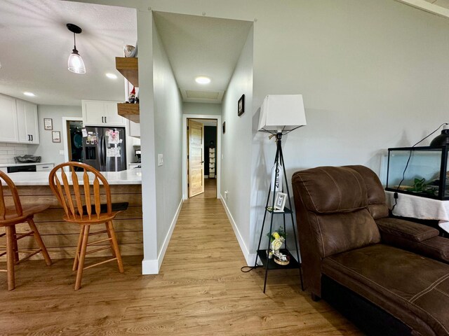 kitchen with pendant lighting, light hardwood / wood-style flooring, stainless steel fridge with ice dispenser, tasteful backsplash, and white cabinetry