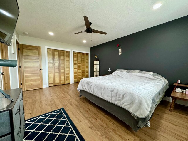 bedroom featuring multiple closets, a textured ceiling, wood-type flooring, and ceiling fan