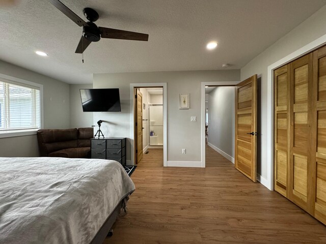 bedroom featuring ensuite bath, ceiling fan, wood-type flooring, and a textured ceiling