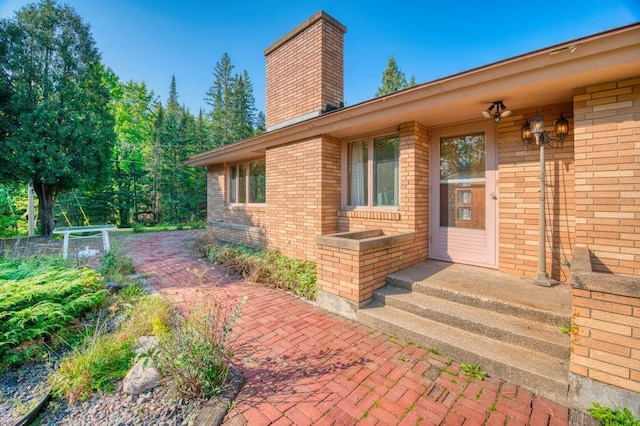 entrance to property with a chimney and brick siding