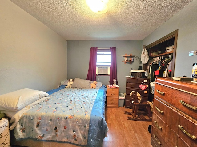 bedroom with a textured ceiling, cooling unit, light hardwood / wood-style floors, and a closet