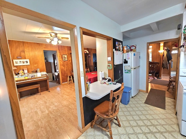 kitchen featuring ceiling fan, white refrigerator, wood walls, a kitchen breakfast bar, and light hardwood / wood-style floors