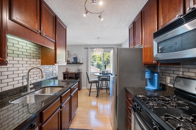 kitchen featuring sink, black range with gas stovetop, backsplash, dark stone countertops, and light wood-type flooring