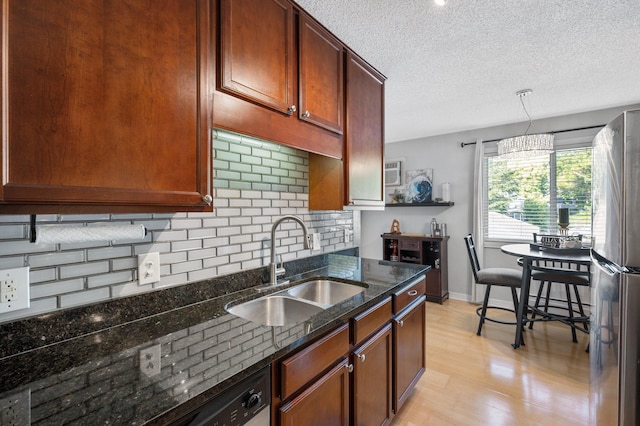 kitchen with stainless steel fridge, light wood-type flooring, dark stone counters, sink, and decorative light fixtures