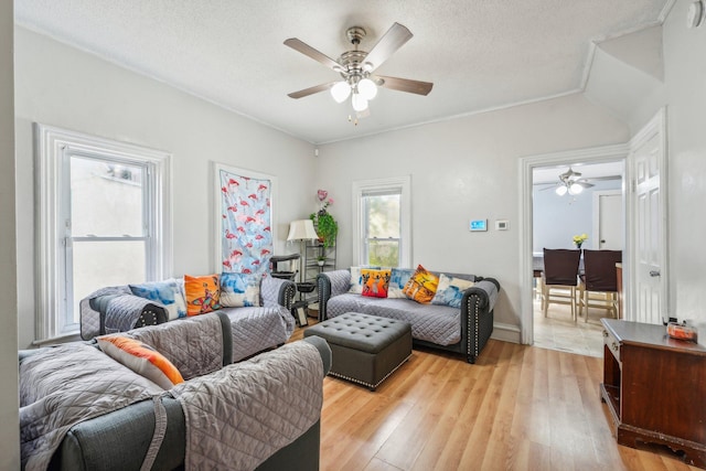 living room with vaulted ceiling, a textured ceiling, light wood-type flooring, and ceiling fan