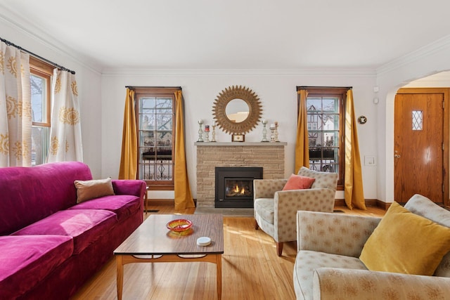 living room with baseboards, ornamental molding, a stone fireplace, wood finished floors, and arched walkways