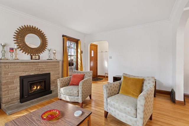 living room featuring crown molding, baseboards, light wood-style flooring, arched walkways, and a glass covered fireplace