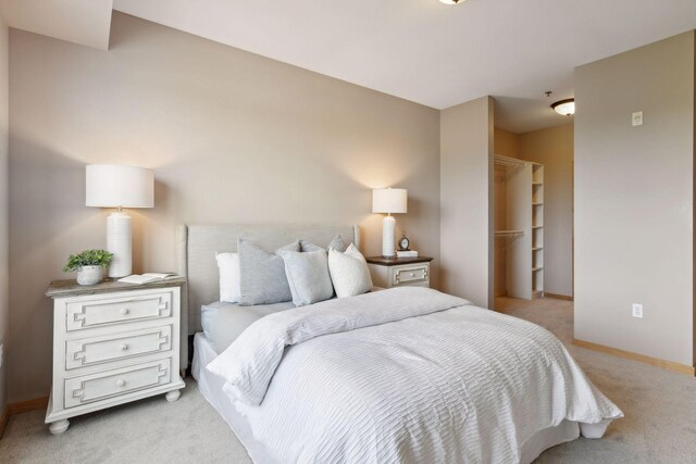 bedroom featuring a walk in closet, baseboards, light colored carpet, and a closet