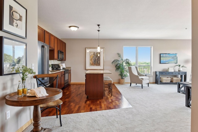 kitchen featuring decorative light fixtures, a kitchen breakfast bar, stainless steel appliances, brown cabinetry, and dark colored carpet