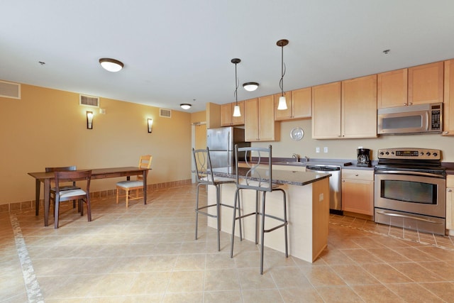 kitchen featuring a kitchen bar, visible vents, light brown cabinetry, a kitchen island, and stainless steel appliances