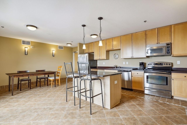 kitchen featuring visible vents, a kitchen island, appliances with stainless steel finishes, and a breakfast bar area